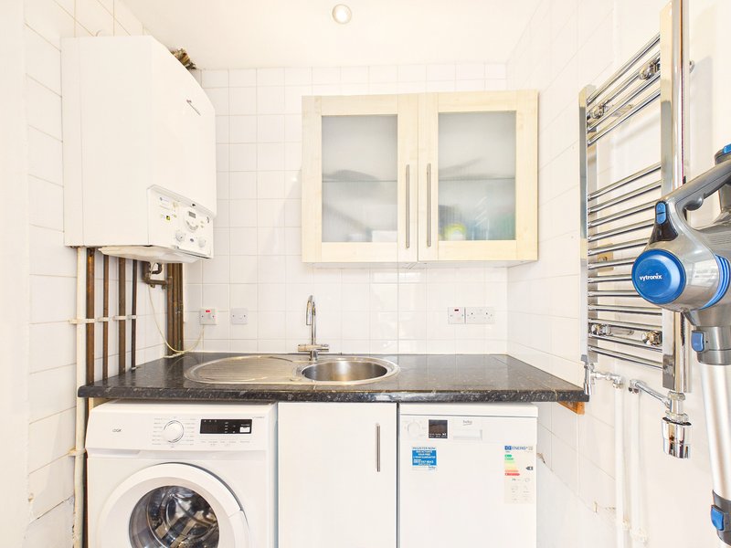 Clean bathroom with sink, washing machine, towel rail and white wall cabinets