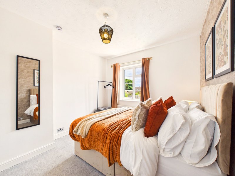 Bright bedroom with double bed, orange throw, white bedding, pendant light and window with garden view