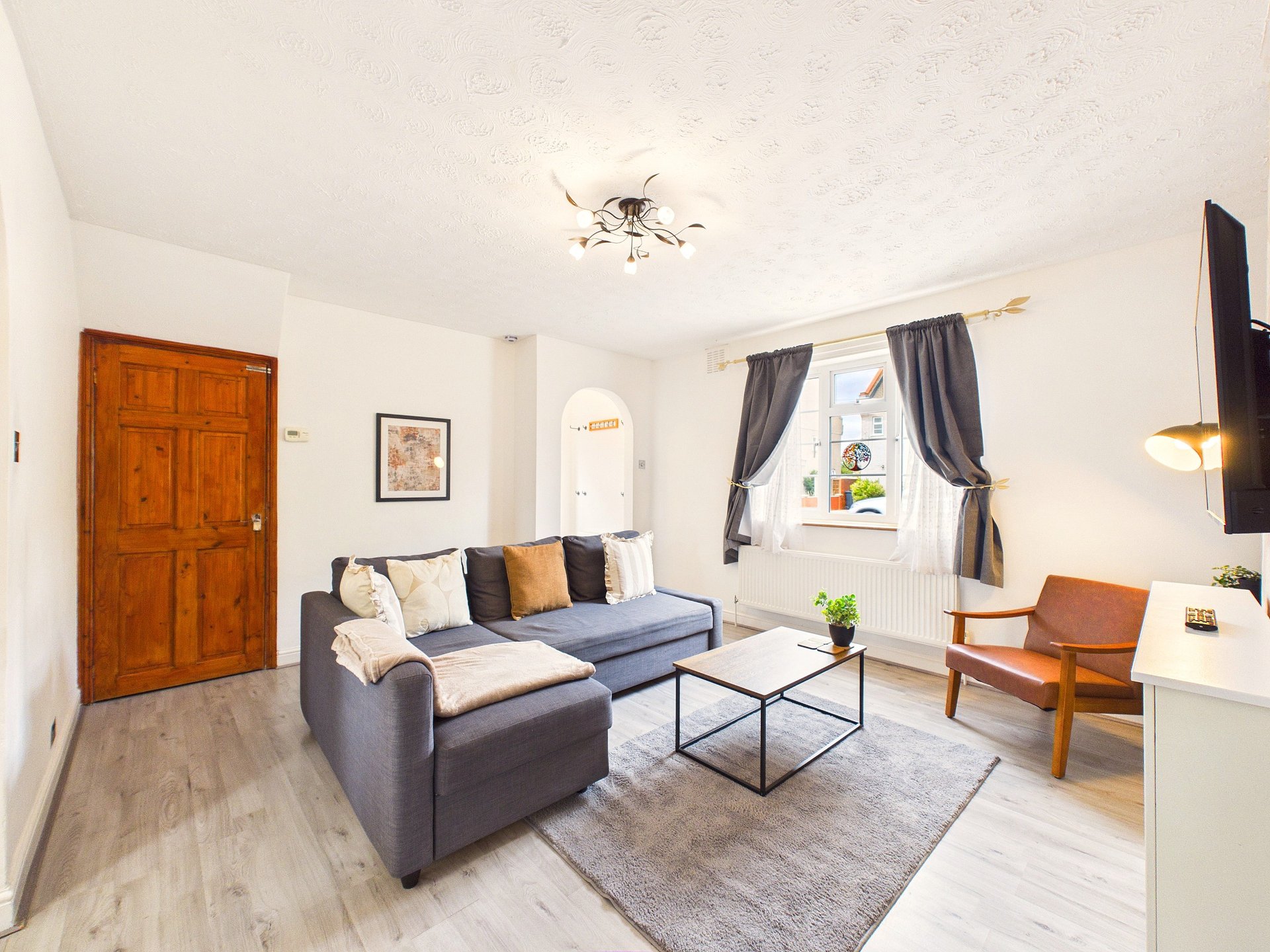 Bright living room with gray sofa, wooden door, window with curtains, and modern furnishings