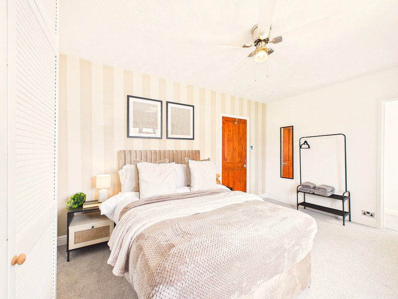 Bright modern bedroom with striped wallpaper, double bed, wooden headboard and clothing rack