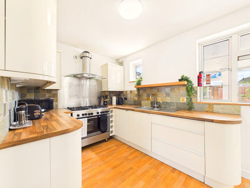 Modern kitchen with white cabinetry, wooden countertops, stainless steel range cooker and orange wooden flooring