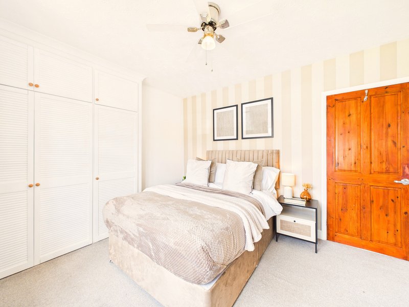 Bright bedroom with double bed, white bedding, wooden wardrobe, and ceiling fan