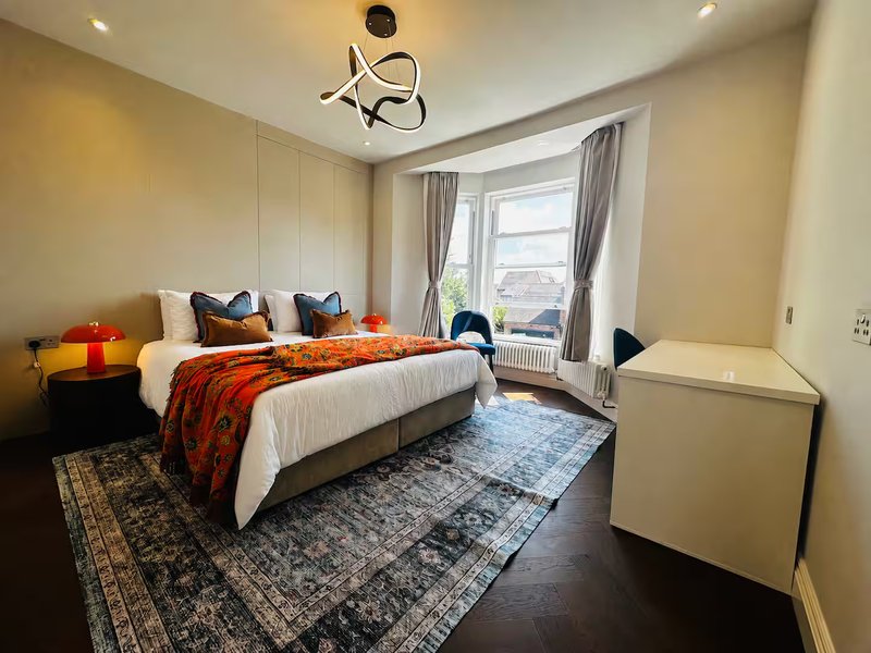 Bright modern bedroom with double bed, orange throw, pendant light, window with curtains and radiator