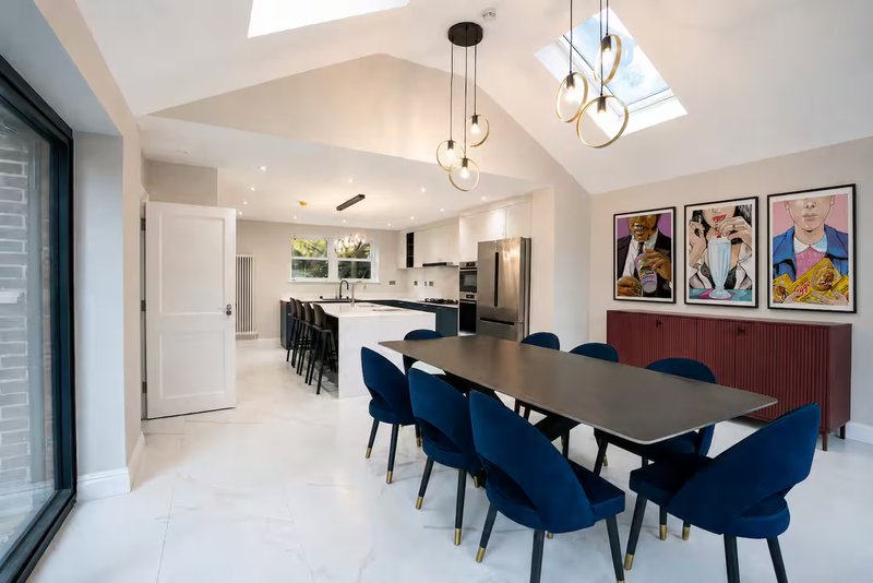 Modern open-plan dining and kitchen area with blue chairs, dark table, and skylight