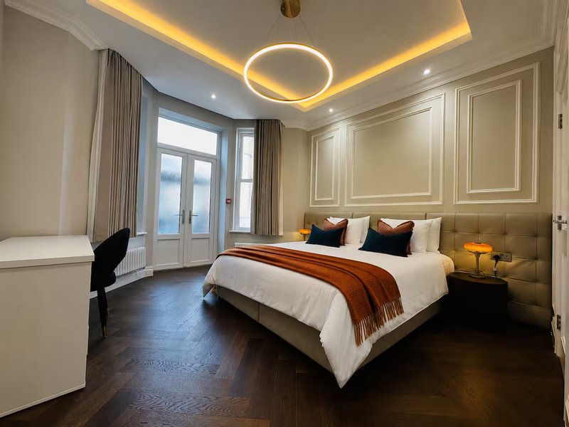 Modern bedroom with king bed, gold ceiling lights, dark wood flooring and glass doors