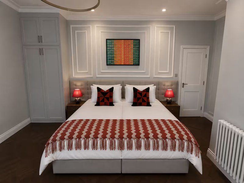 Modern bedroom with double bed, red patterned throw, decorative pillows and wall-mounted artwork