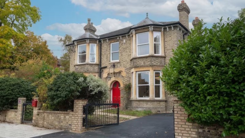 Stone Victorian house with red door, bay windows, driveway and front garden