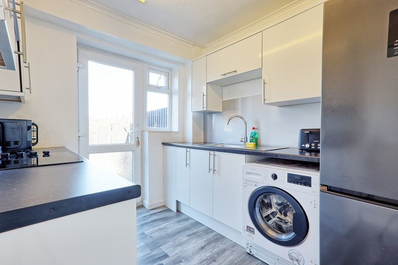 Modern kitchen with white cabinets, washing machine, and glass door to garden