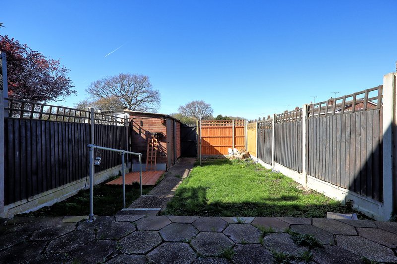 Rear garden with paved patio, green lawn, wooden fencing and storage sheds
