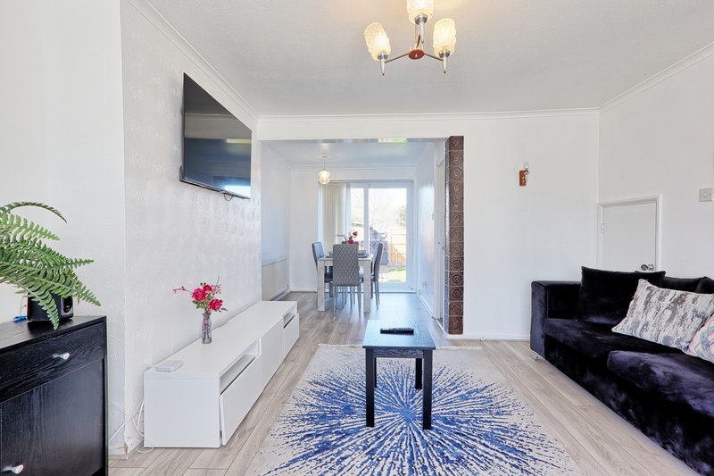 Modern open-plan living room with black sofa, wall-mounted TV, white storage unit and blue rug