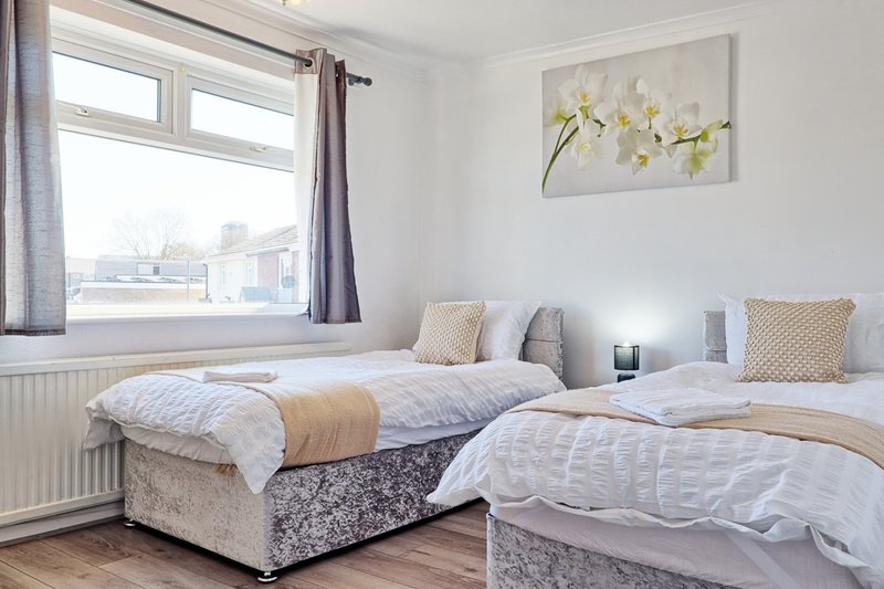 Bright bedroom with two single beds, pillows, window with curtains and flower artwork