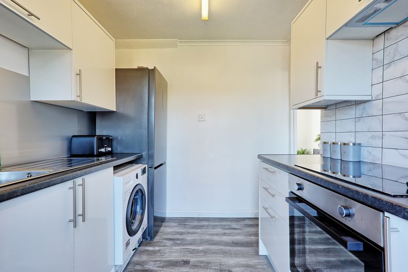 Modern galley kitchen with white cabinets, black countertops, integrated washing machine and oven