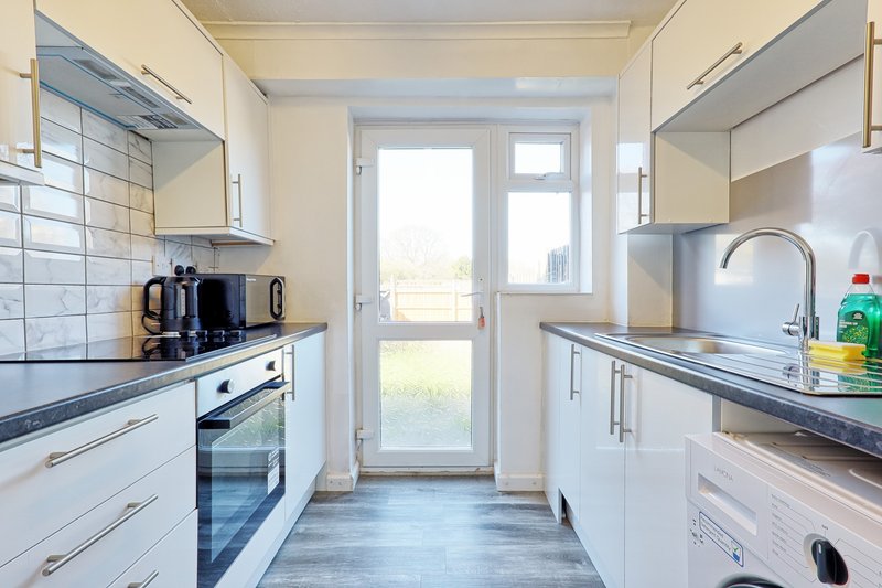 Modern galley kitchen with white cabinetry, stainless steel appliances and glass door to garden