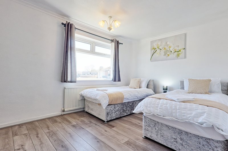 Bright bedroom with two single beds, wooden floor, window and ceiling light