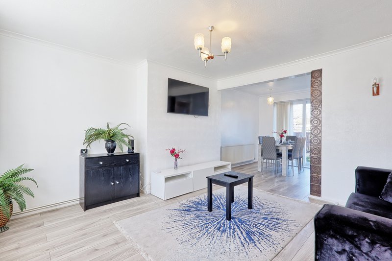 Modern living room with light wood flooring, mounted TV, black cabinet with plants, and open-plan layout