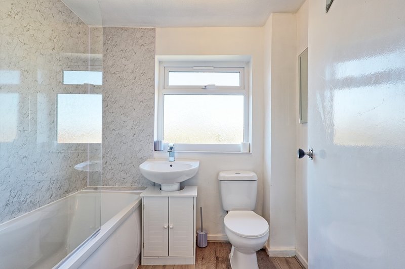 Clean bathroom with bathtub, pedestal sink, toilet, and window with natural light