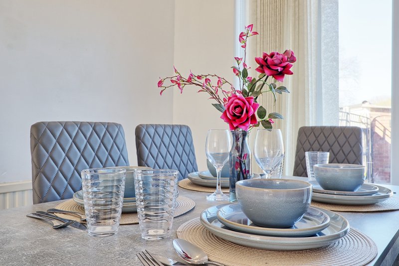 Dining table set with place settings, glasses, and pink flowers in vase