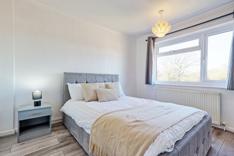 Bright bedroom with grey upholstered bed, white bedding, wooden floor and pendant light fixture