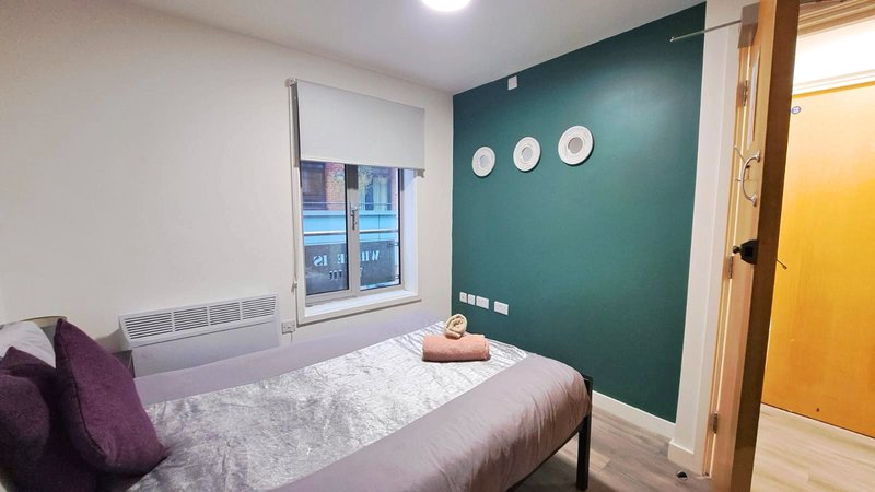 Bedroom with single bed, teal accent wall, window, purple cushions and yellow door
