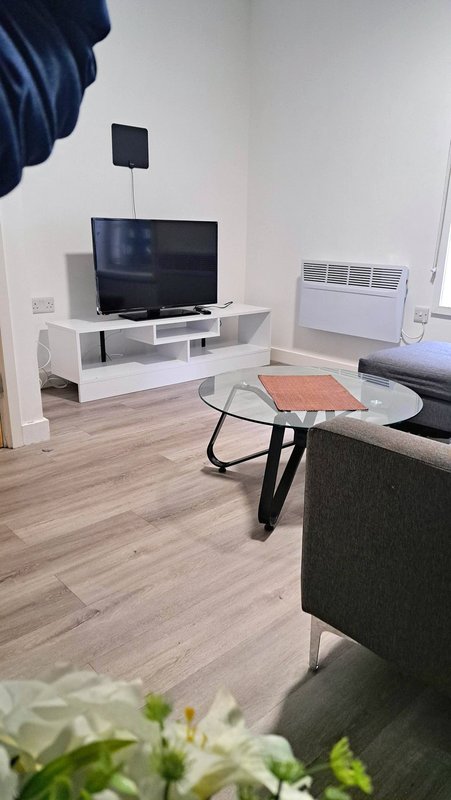 Modern living room with TV on white stand, round glass table, grey sofa and wooden flooring