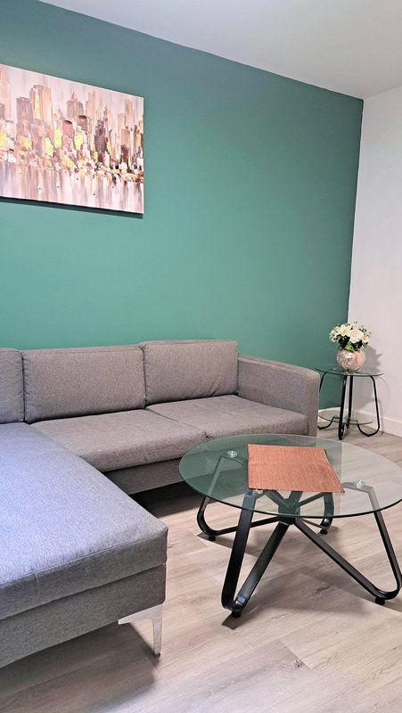 Modern living room with grey sofa, glass coffee table, teal accent wall and artwork