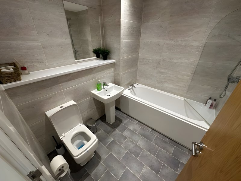 Modern bathroom with toilet, pedestal sink, bathtub, mirror and tiled walls