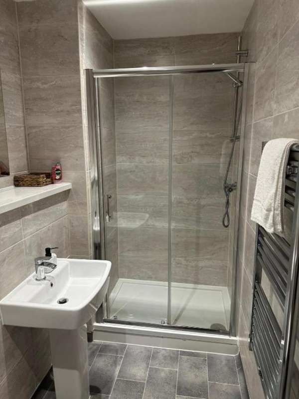 Modern bathroom with glass shower enclosure, white basin sink and heated towel rail
