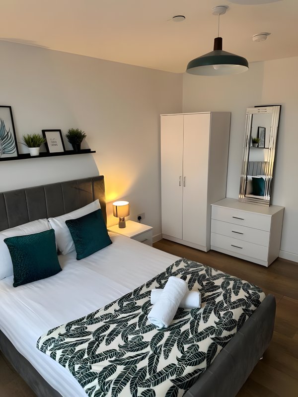Modern bedroom with double bed, teal pillows, pendant lamp and white wardrobes