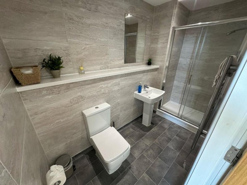 Modern bathroom with toilet, pedestal sink, shower enclosure and neutral tile walls