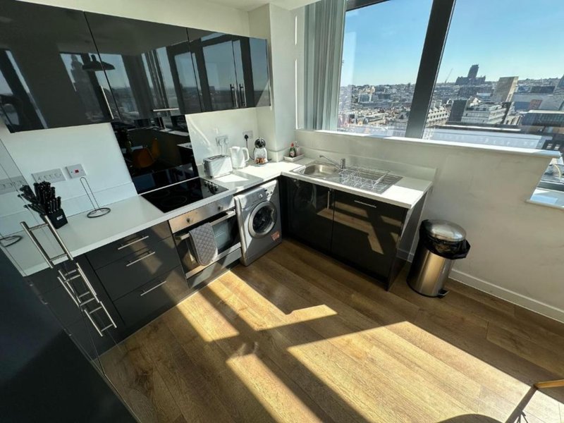 Modern kitchen with black cabinetry, washing machine, and city views from large windows
