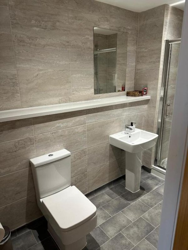 Modern bathroom with toilet, pedestal sink, mirror and tiled walls