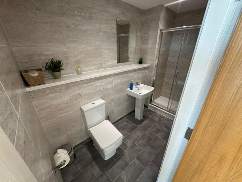 Modern bathroom with toilet, pedestal sink, mirror, shower enclosure and tiled walls