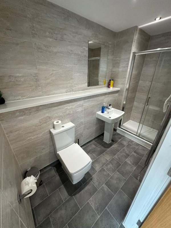 Modern bathroom with toilet, pedestal sink, shower enclosure and gray tile walls