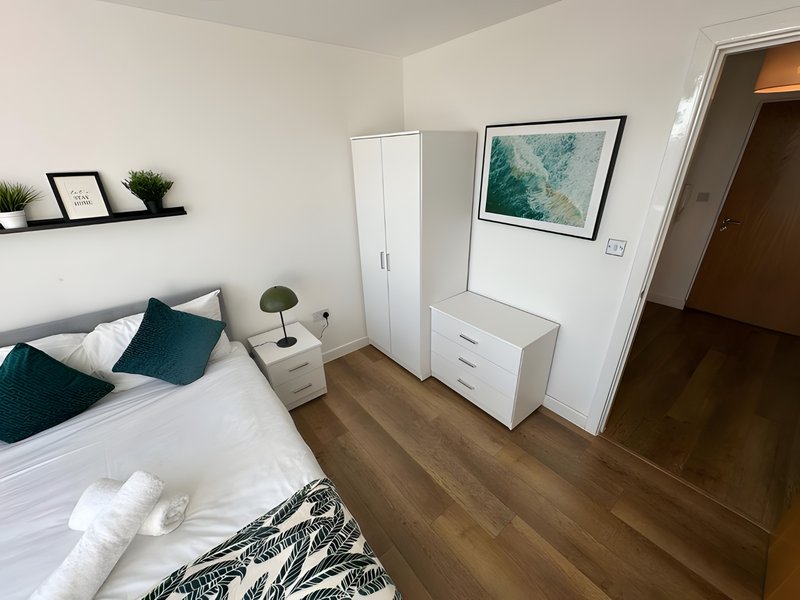 Bedroom with double bed, teal cushions, wooden floor, white furniture and wall art