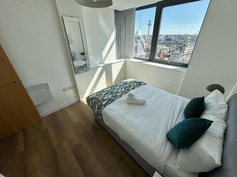 Bright bedroom with double bed, city view from large window, wooden floor and mirror