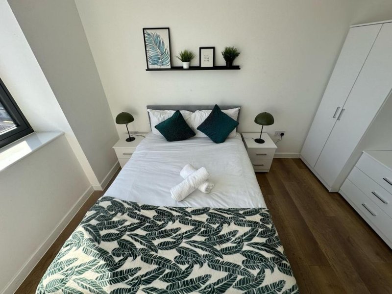 Modern bedroom with double bed, green cushions, bedside lamps, wooden floor and wall shelving