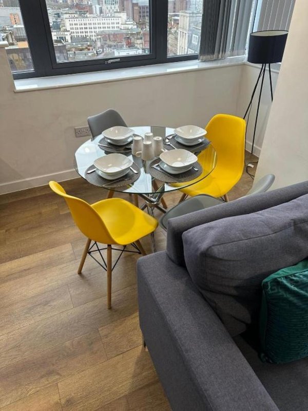 Dining area with round table, yellow chairs, place settings, and city views from windows
