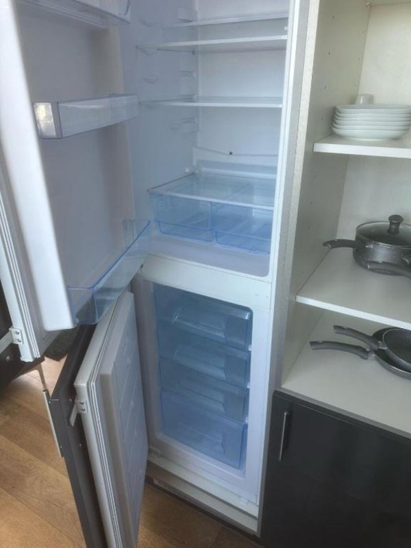 Open refrigerator with empty shelves and kitchen cabinets with dishes and cookware