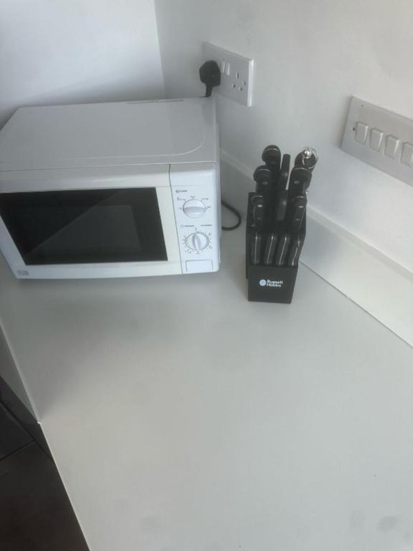 Kitchen counter with white microwave and black knife block next to electrical outlets