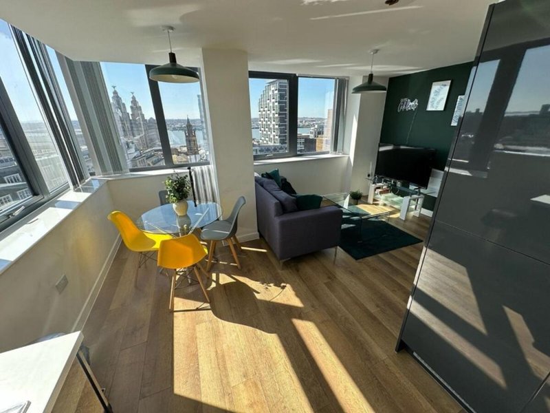 Modern apartment living area with dining table, sofa, and floor-to-ceiling windows overlooking city skyline