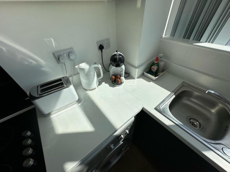 Compact kitchen with white countertop, electric kettle, coffee maker, and stainless steel sink