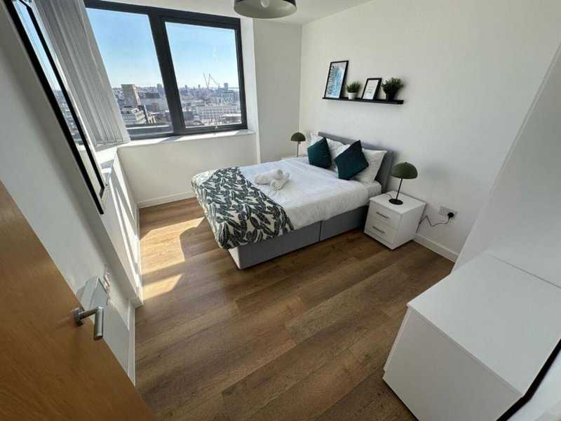 Modern bedroom with double bed, wooden floor, city view window, and bedside furniture