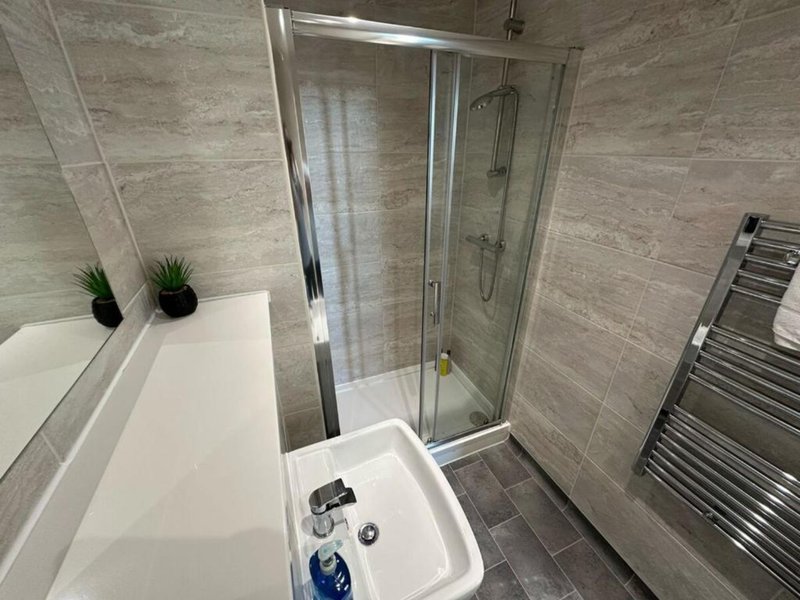 Modern bathroom with shower enclosure, bathtub, heated towel rail and grey tile walls