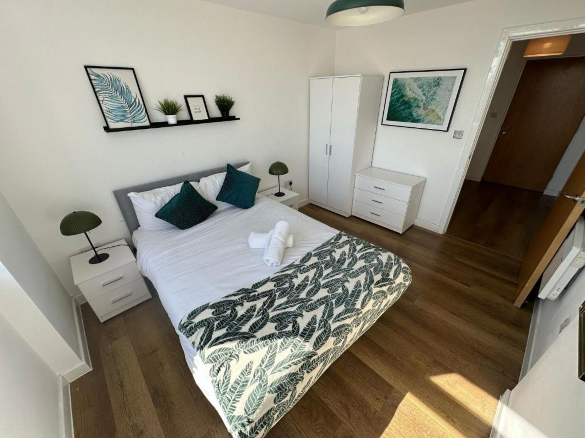 Bright bedroom with double bed, white bedding, dark cushions, wooden flooring and wardrobe