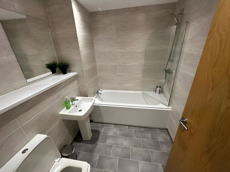 Modern bathroom with white bath, shower enclosure, sink, toilet and grey tile flooring