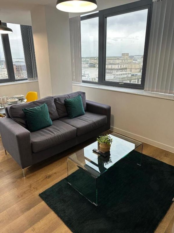 Modern living room with dark sofa, glass coffee table, city view windows and wooden flooring