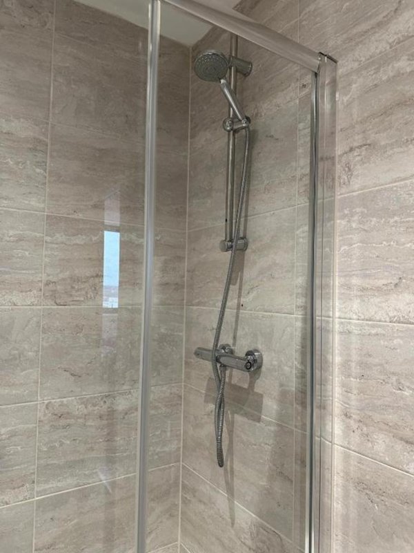 Modern bathroom shower enclosure with glass door and chrome fixtures on tiled walls