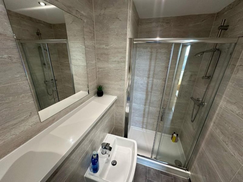 Modern bathroom with gray tile walls, white vanity sink, mirror, and glass shower enclosure