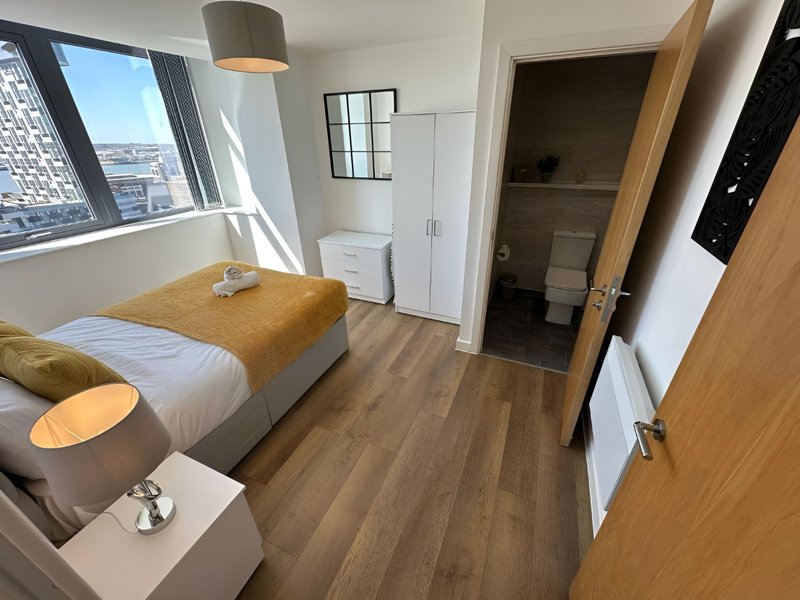 Modern bedroom with single bed, wooden flooring, city views from window, and en-suite bathroom