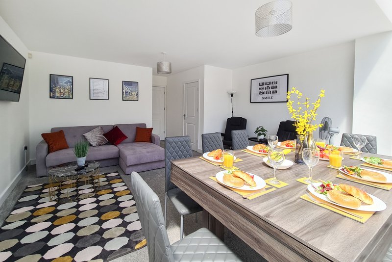 Open-plan living and dining room with purple sofa, patterned rug, dining table set for six with yellow accents